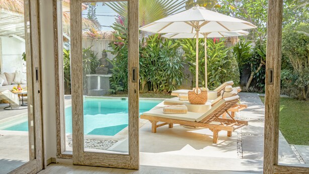 Un espace aménagé au bord de la piscine, avec des chaises longues en bois, un grand parasol et une vue sur la piscine.