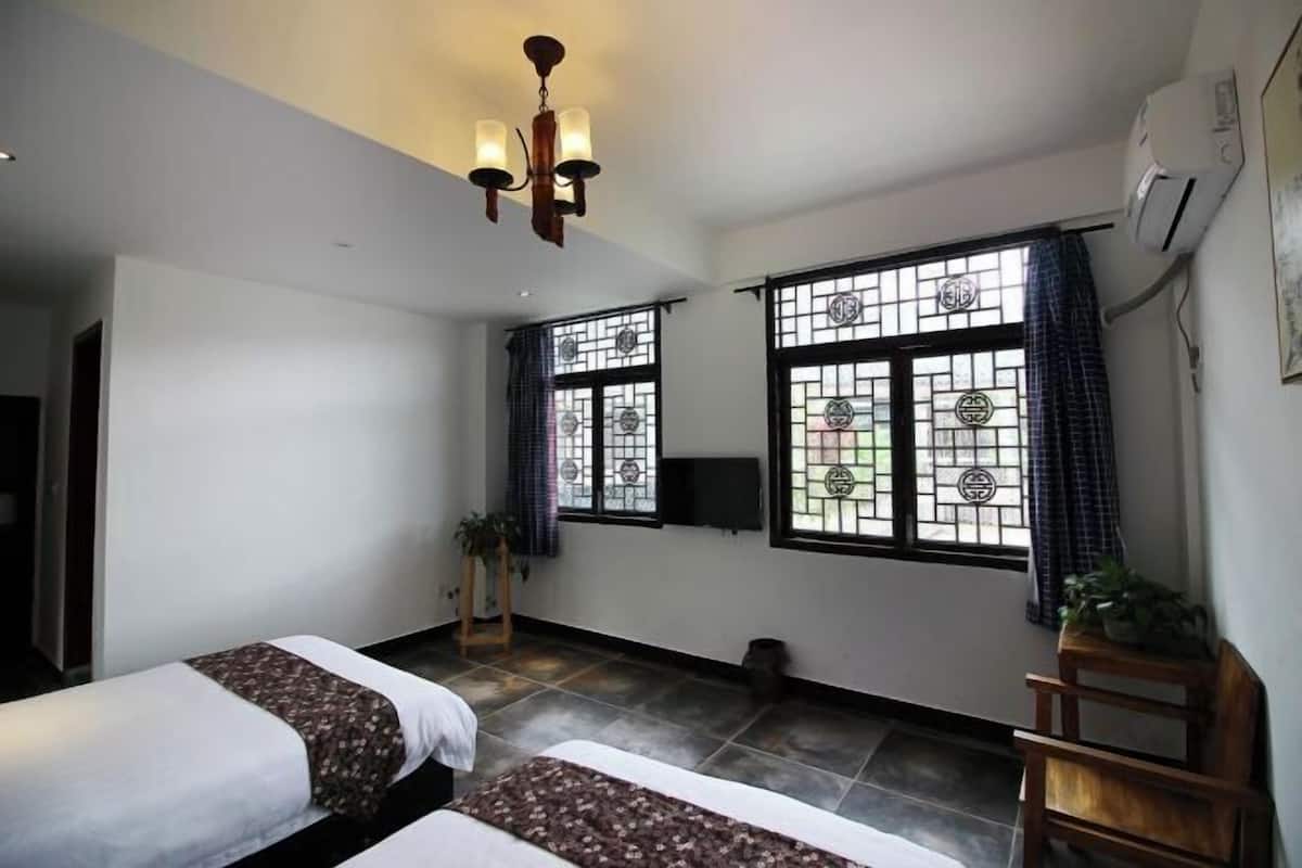 A hotel room with two beds, a TV, a chandelier, and large windows with curtains.