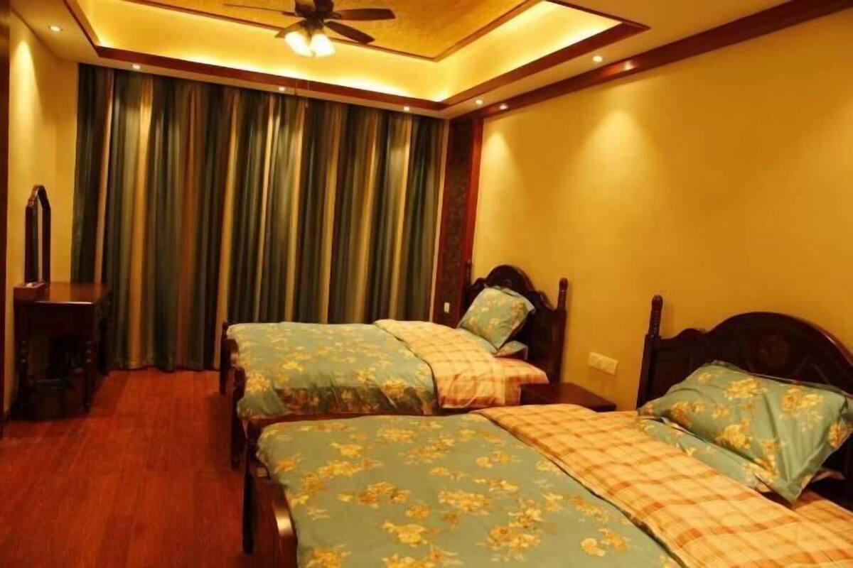 A hotel room with two beds, a ceiling fan, a mirror, and a large window with curtains.