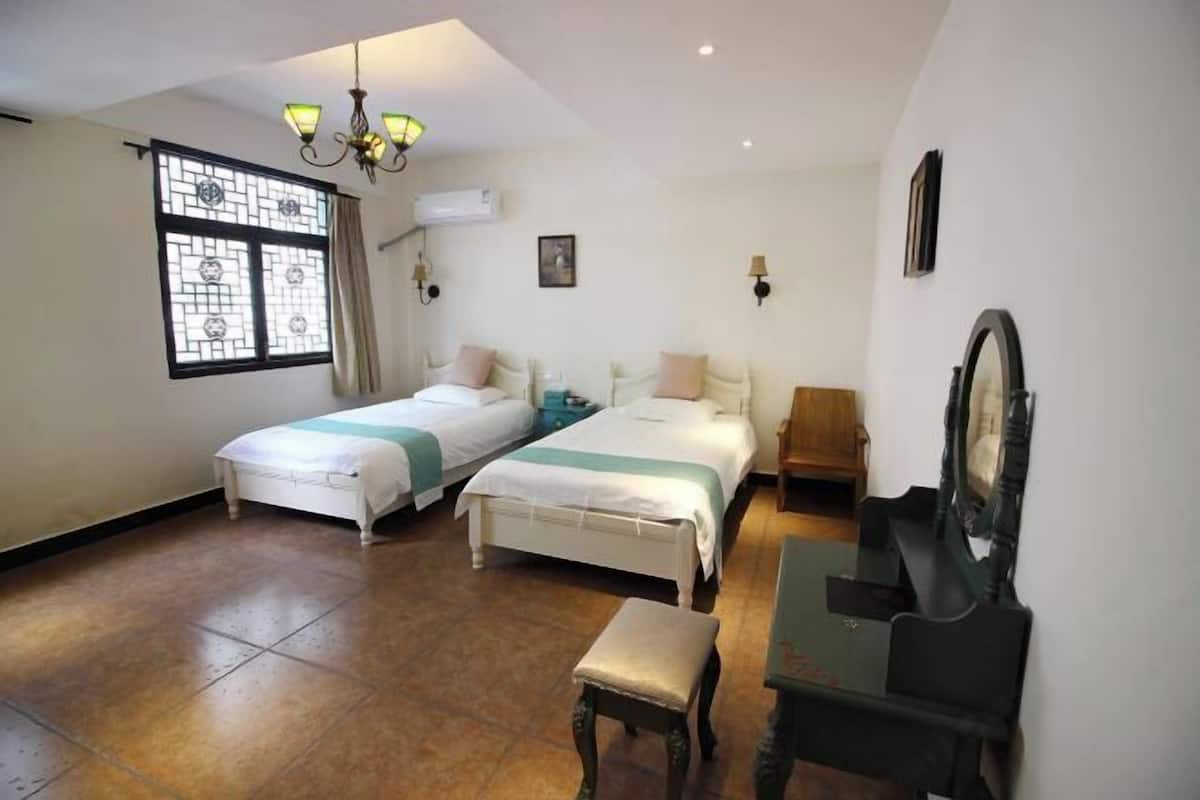 A hotel room with two beds, a piano, a bench, and a large mirror.