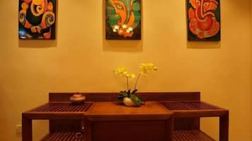 A wooden dining table with a vase of yellow flowers, flanked by three framed artworks on the wall.