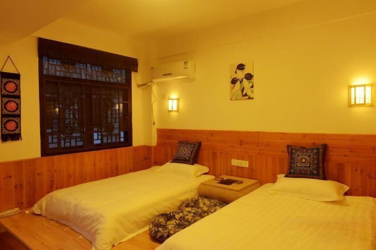 A room with two beds, a window with a view, wall-mounted lights, and a wall decoration.