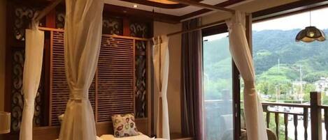 Un dormitorio con cama con dosel, un balcón con vistas a zonas verdes y un ventilador de techo.