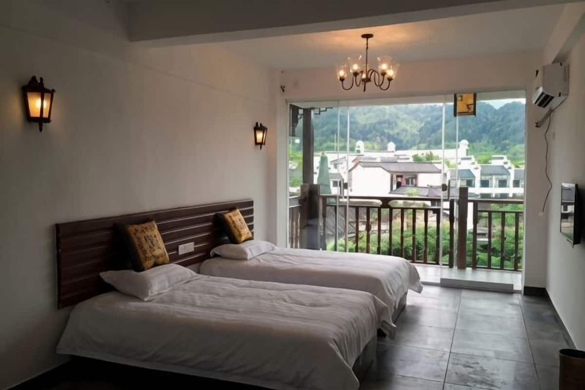 A hotel room with two beds, a balcony with a view of the mountains, and a chandelier.