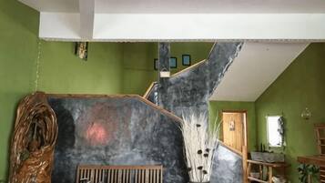 Una habitación con techo inclinado, un banco de madera, un jarrón grande con ramas y una escalera.