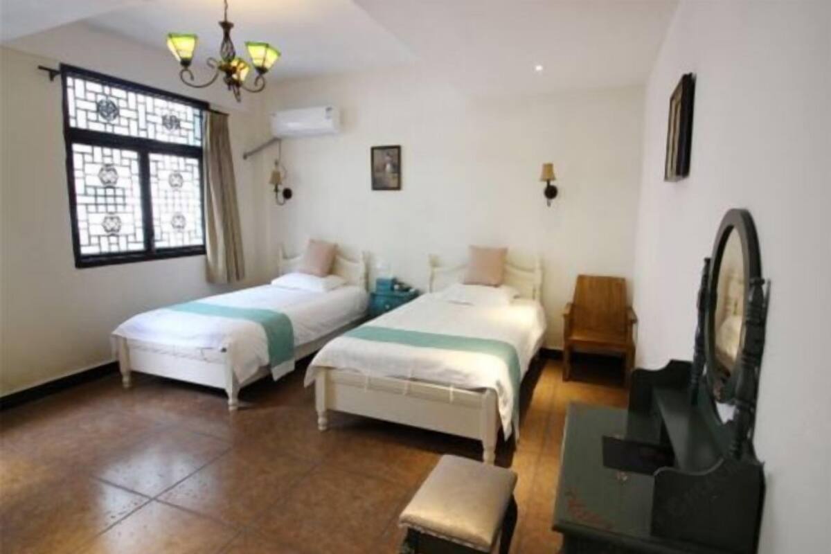 A room with two beds, a bench, a piano, and a window with a decorative grille.