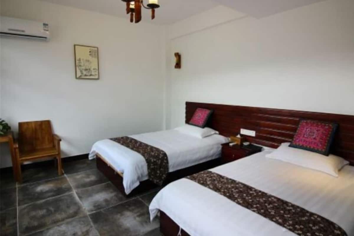 A hotel room with two beds, a wooden chair, a nightstand, and a wall-mounted air conditioner.