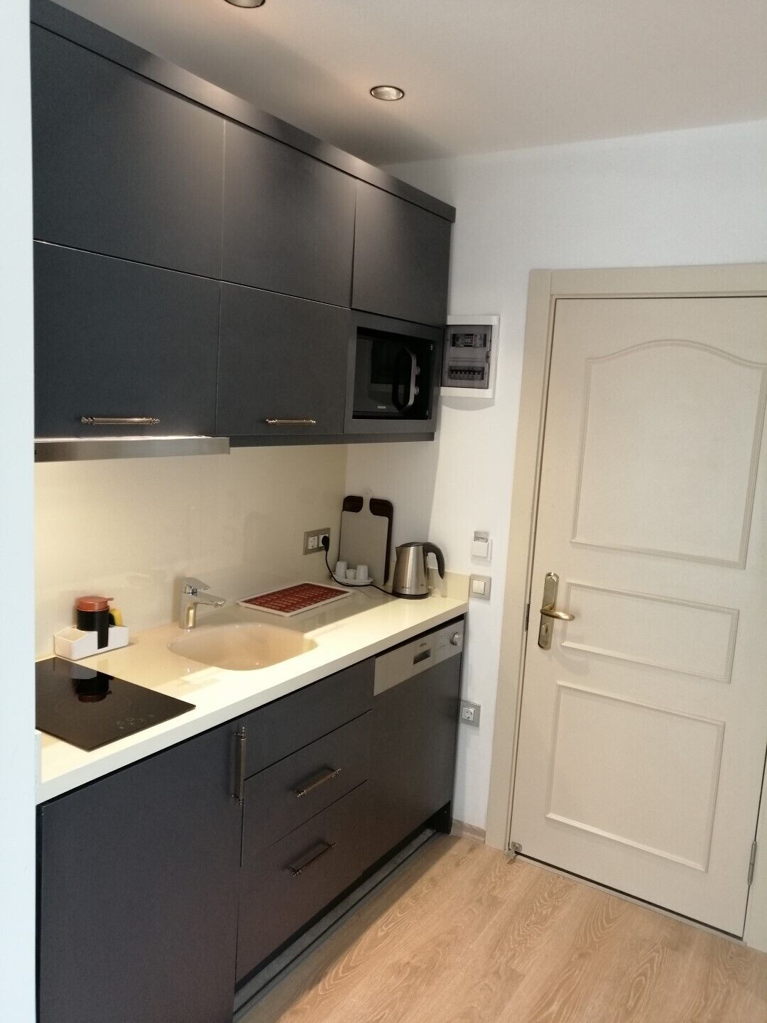 A modern kitchen with dark cabinets, a white countertop, a built-in microwave, and a coffee machine.