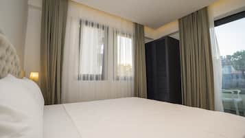 Quarto de hotel com uma cama grande, janela com cortinas leves, vista da cidade e varanda com mesa e cadeiras.