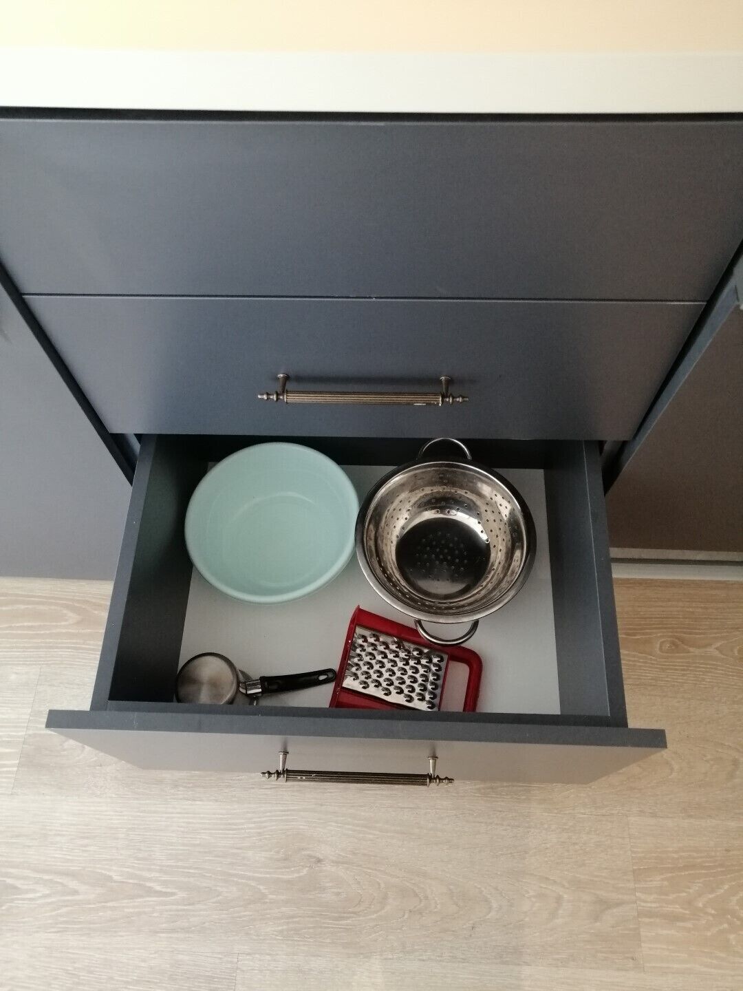 A drawer with a blue plate, a metal colander, and a red grater.