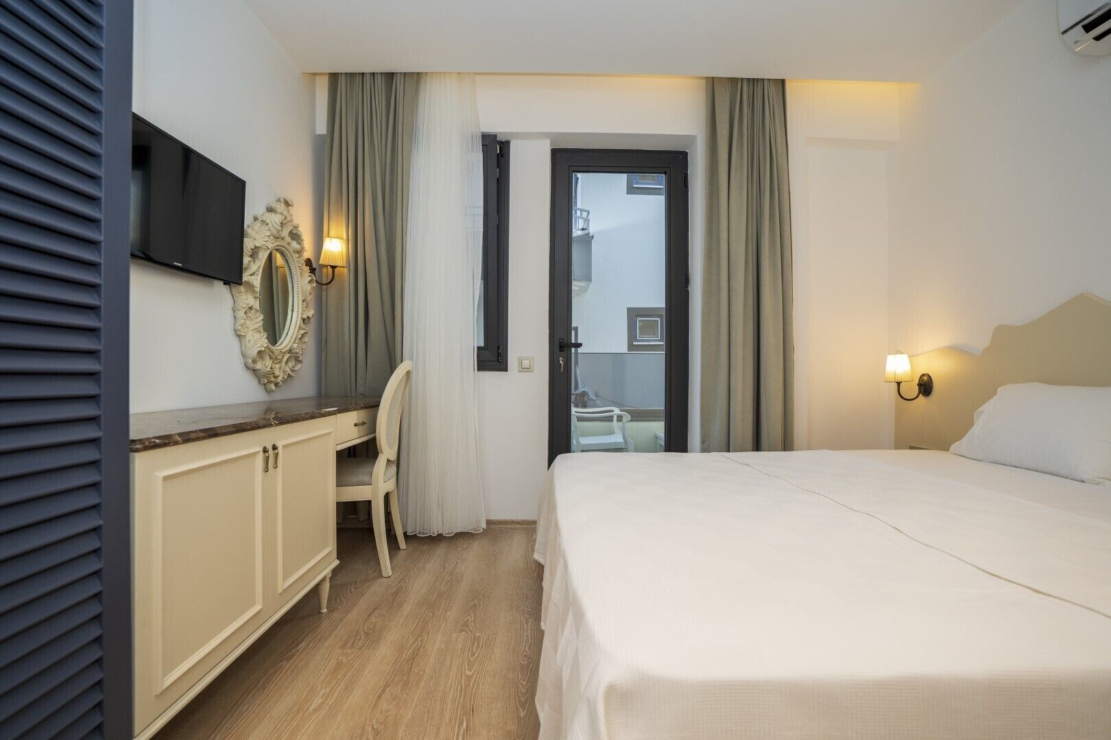 A hotel room with a bed, a desk, a chair, a television, and a door leading to a balcony.