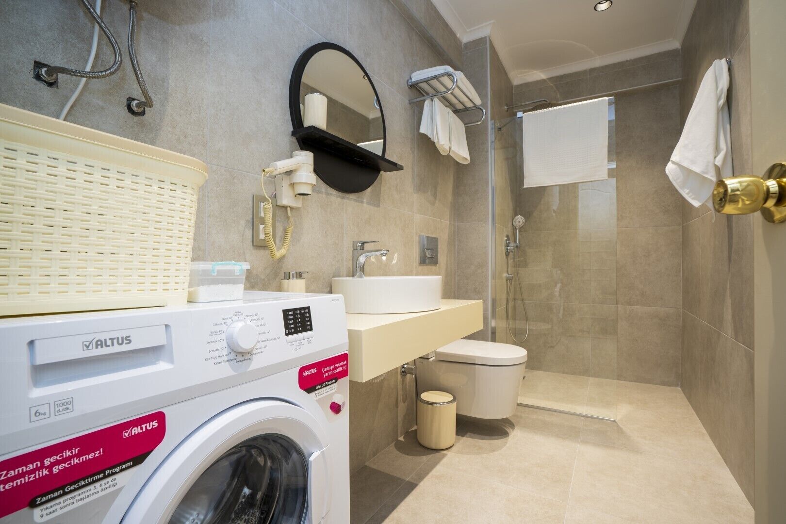 A modern bathroom with a washing machine, sink, toilet, and shower.