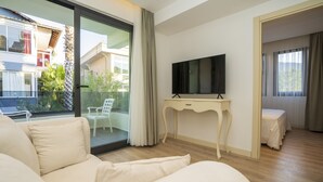 Una habitación de hotel moderna con una cama grande, un televisor sobre una consola blanca y un balcón con vistas al exterior.