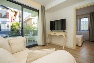Una habitación de hotel moderna con una cama grande, un televisor sobre una consola blanca y un balcón con vistas al exterior.
