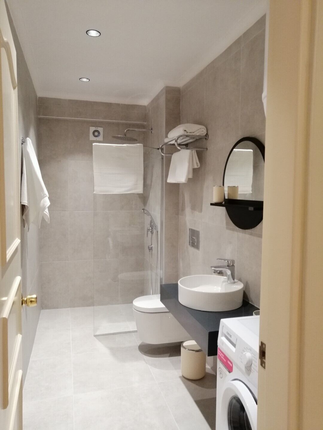 A modern bathroom with a toilet, sink, shower, and a washing machine.