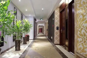A hotel corridor with potted plants, wooden flooring, and doors leading to rooms. - The westside Lancaster Hotel (Xichong)