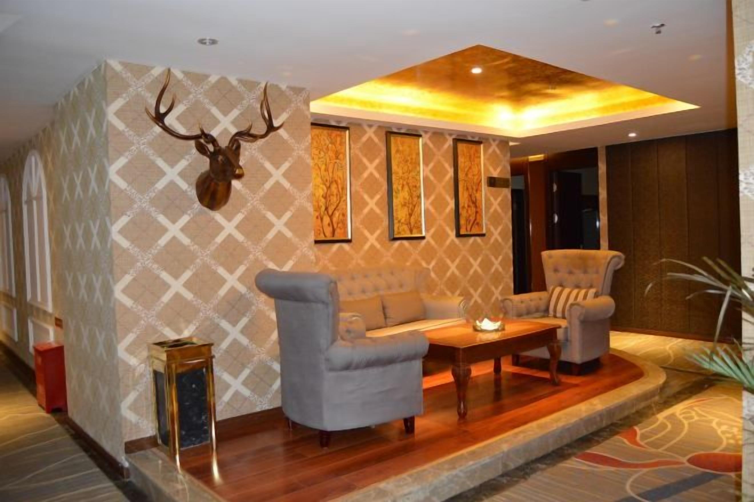 Een kamer met een behang met patroon, een bank, twee fauteuils, een salontafel en een op de muur bevestigd hertenhoofd.