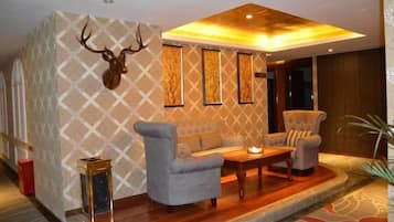 Een kamer met een behang met patroon, een bank, twee fauteuils, een salontafel en een op de muur bevestigd hertenhoofd.