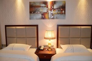 Une chambre d’hôtel avec deux lits, une table de chevet avec une lampe et un tableau au mur.