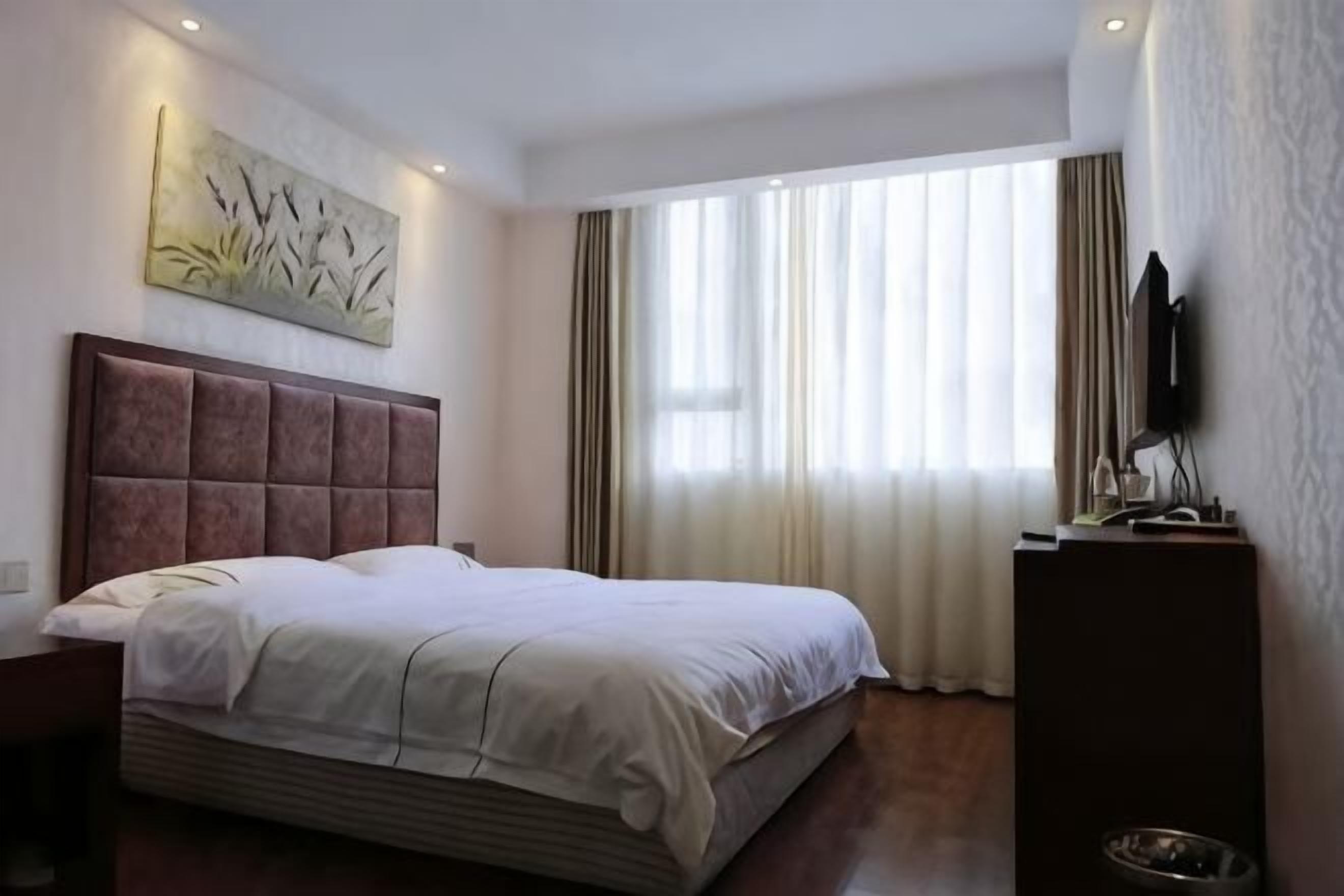 Hotellihuone, jossa on suuri sänky, taulutelevisio ja taulu seinällä.