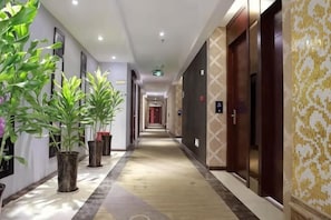 Un couloir d’hôtel agrémenté de plantes en pot, doté d’un plancher en bois et de portes recouvertes d’un papier peint à motifs.