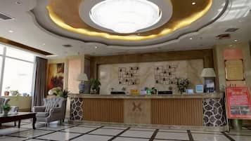 Zona d'entrada d'un hotel amb un disseny modern, que inclou un taulell de recepció, una zona de seients i una gran lluminària circular al sostre.