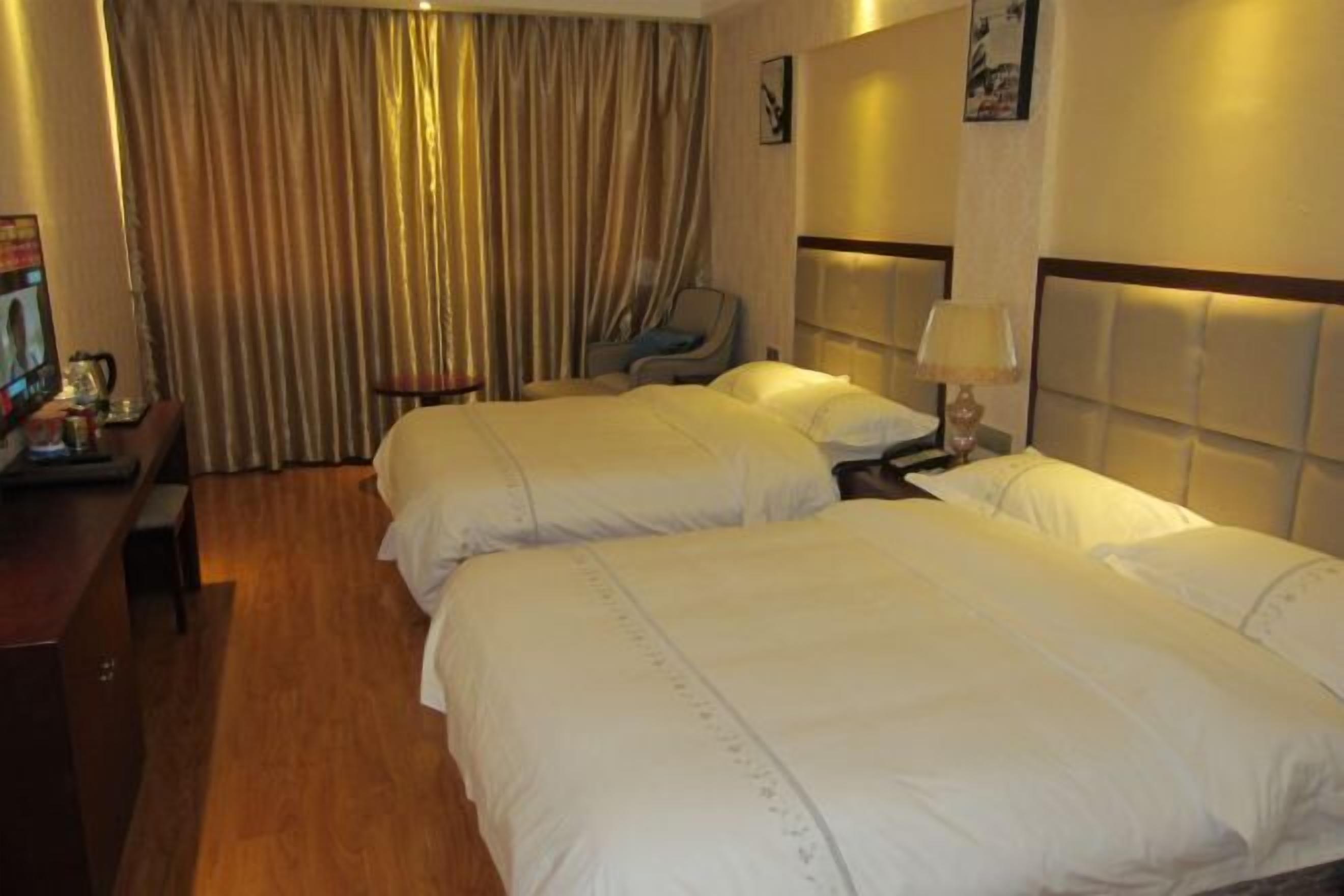 Quarto de hotel com duas camas, uma escrivaninha, uma cadeira e uma janela grande com cortinas.
