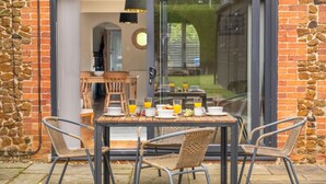 Un comedor con una mesa dispuesta para dos, sillas de mimbre y una puerta de cristal que da a un patio.