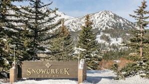 A sign for Snow Creek Resort surrounded by snow-covered trees and mountains.