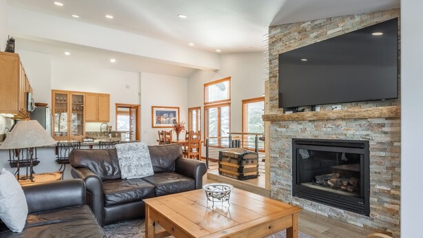 A spacious living room with a fireplace, leather sofa, wooden coffee table, and a dining area with wooden cabinets and a chandelier.
