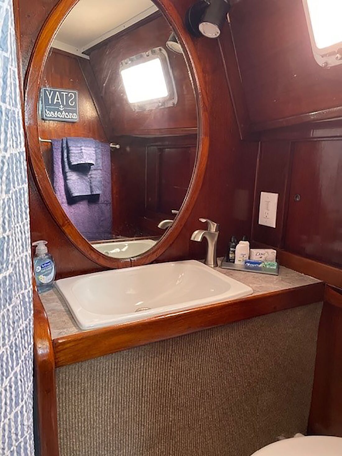 A compact bathroom with a wooden vanity, a large mirror, and a small window.