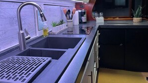 Una cocina moderna con un lavamanos de acero inoxidable, una placa de cocción integrada y una ventana sobre el lavamanos.