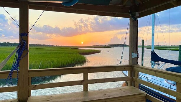 Una terraza de madera con vistas a la puesta de sol sobre un río y campos.