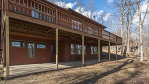 A two-story wooden cabin with a balcony, large windows, and a deck area. - ★Cabin: Pet/Family Friendly, Hot Tub, Large Deck★ (Berkeley Springs)