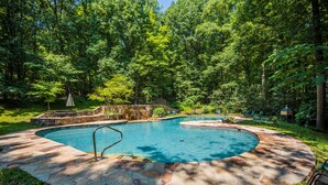 A swimming pool with a stone deck, surrounded by a forested area. - ★Cabin: Pet/Family Friendly, Hot Tub, Large Deck★ (Berkeley Springs)