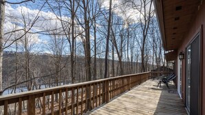 A wooden deck with a railing overlooking a forested area and a body of water. - ★Cabin: Pet/Family Friendly, Hot Tub, Large Deck★ (Berkeley Springs)