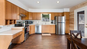A modern kitchen with wooden cabinets, stainless steel appliances, and a large window. - ★Cabin: Pet/Family Friendly, Hot Tub, Large Deck★ (Berkeley Springs)