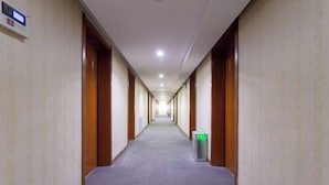A long, narrow hotel corridor with carpeted floors, wooden doors, and a trash bin. - Qingzhu·Junyuan Business Hotel (Binzhou University Branch) (Binzhou)