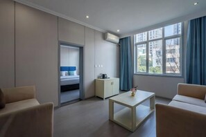 A modern hotel room with a bed, a small table, a cabinet, and a window with curtains.