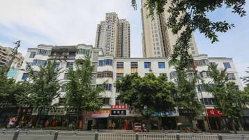 A multi-story building with commercial establishments on the ground floor, surrounded by trees and a clear sky.