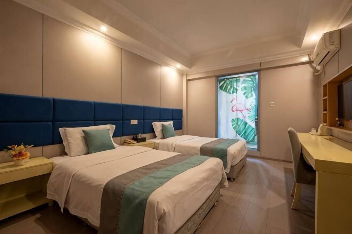 A hotel room with two beds, a desk, a chair, and a window with a tropical view.