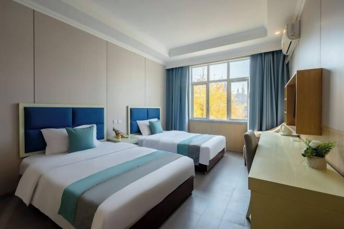 A hotel room with two beds, a desk, and a window with curtains.