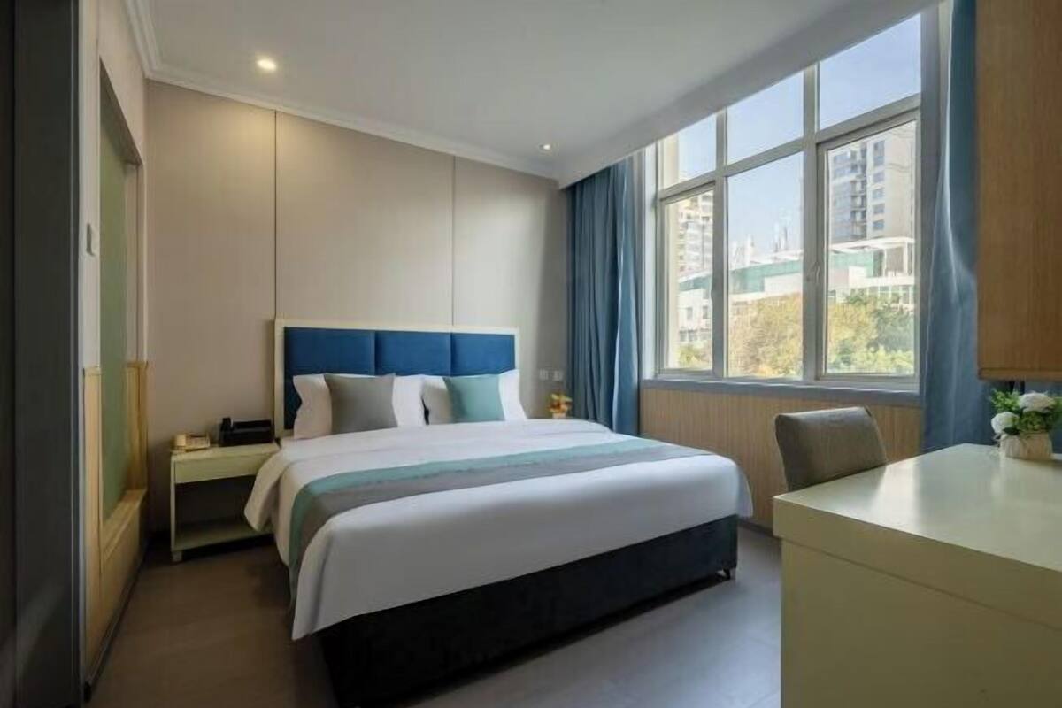 A modern hotel room with a large bed, a desk, and a window with a city view.