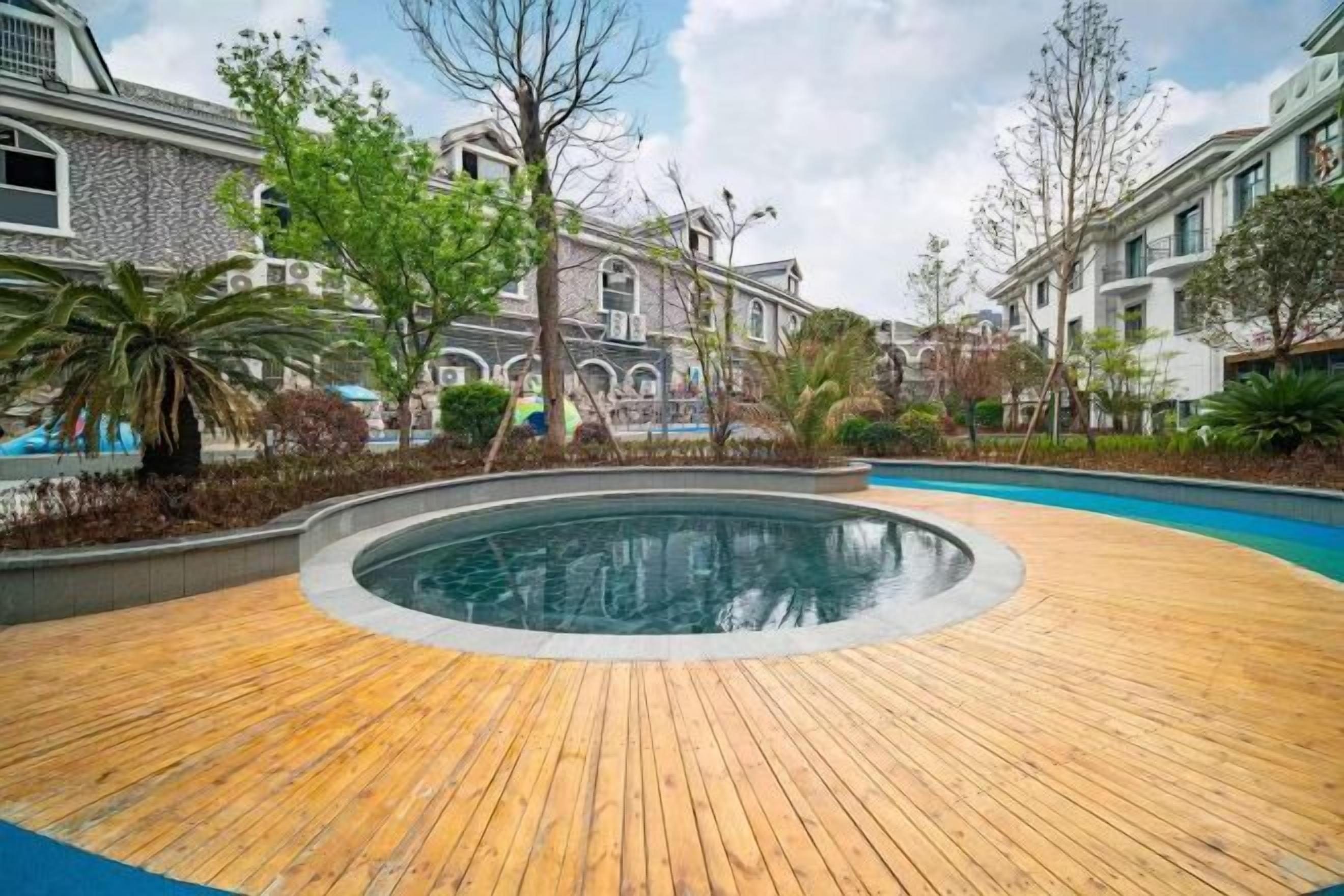A wooden deck surrounding a circular pool with a stone wall, surrounded by trees and buildings.