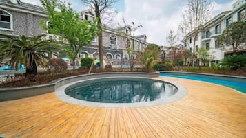 A wooden deck surrounding a circular pool with a stone wall, surrounded by trees and buildings.