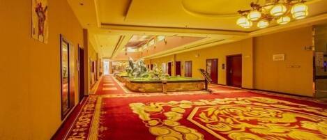 A hotel corridor with a red carpet, framed artwork on the walls, and a chandelier.