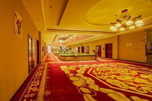 Un pasillo de hotel con alfombra roja, obras de arte enmarcadas en las paredes y un candelabro.