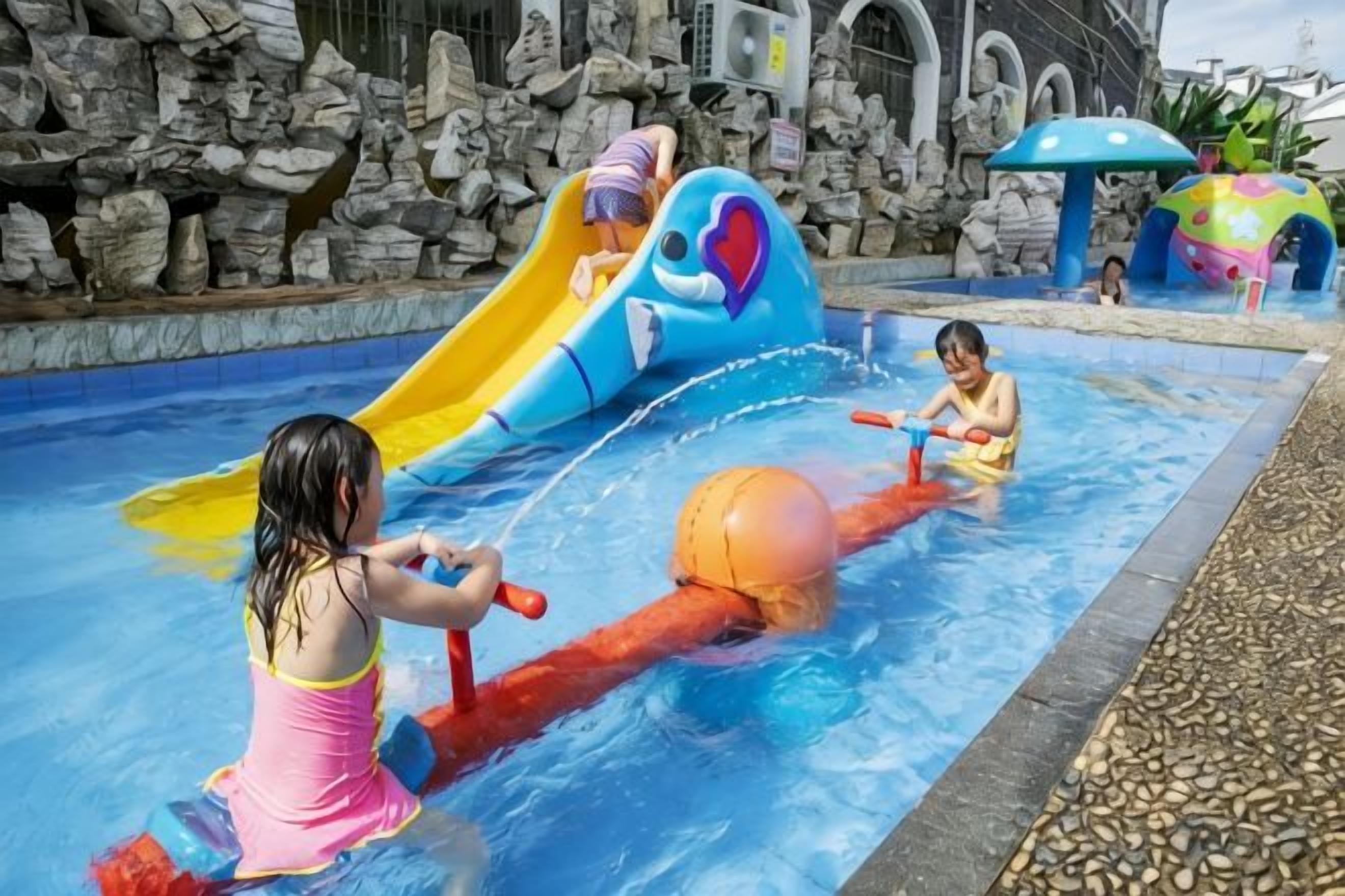 Children playing in a water park pool with slides and play structures.