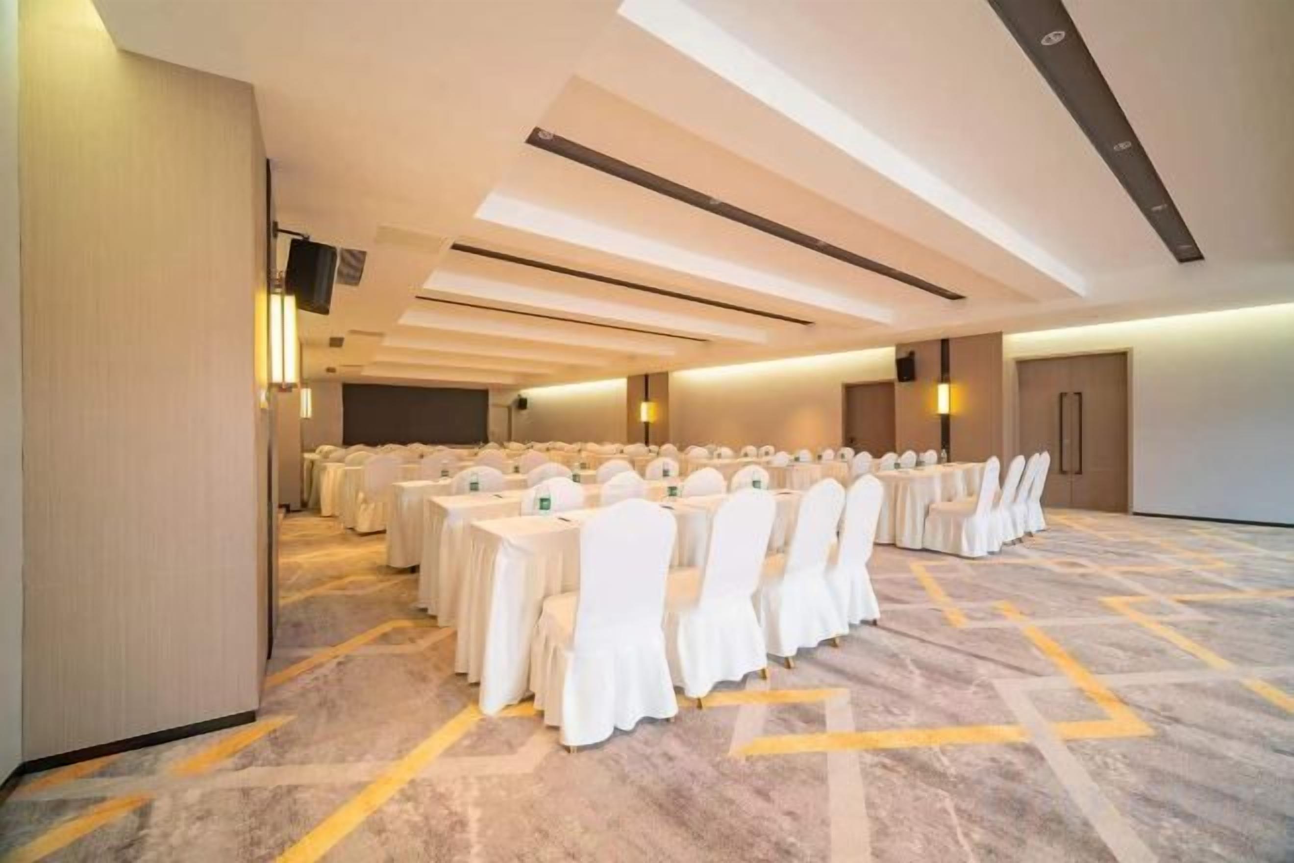 Uma sala de conferências com fileiras de mesas e cadeiras, piso coberto por carpete e design moderno no teto.