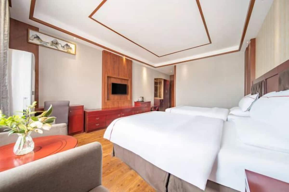 Ein Hotelzimmer mit einem großen Bett, einem an der Wand befestigten Fernseher, einer Holzkommode und einem Schreibtisch mit Stuhl.